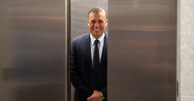Devon Archer rides an elevator, wearing a black suit.