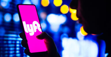 A woman's silhouette holds a smartphone with the Lyft logo displayed on the screen.