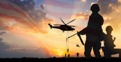 Silhouette of soldier and other soldiers rappelling from a helicopter over the United States flag at sunset