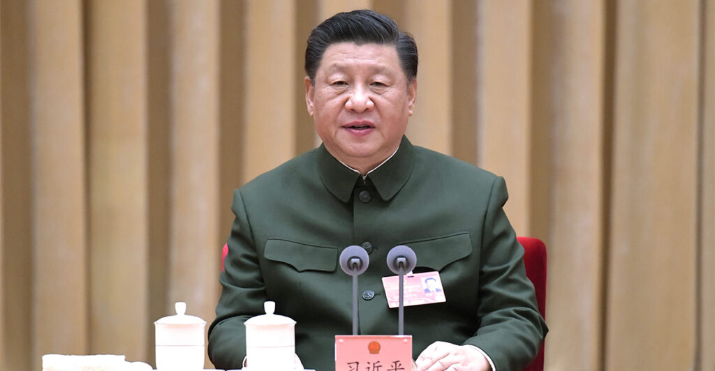 Chinese President Xi Jinping in green military uniform sitting in front of microphones