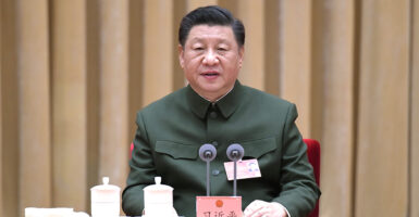 Chinese President Xi Jinping in green military uniform sitting in front of microphones