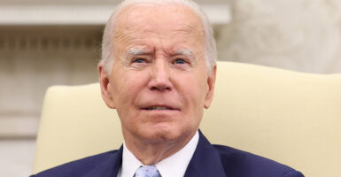 President Joe Biden looks strait ahead while sitting in a chair in the Oval Office.