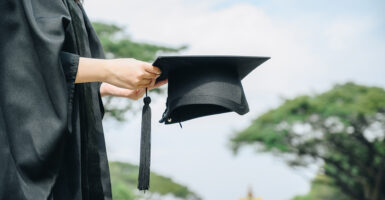 A woman in a graduation gown holds her graduation cap in her hands in front of her.