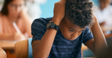 Black male student holds head in hands in classroom.