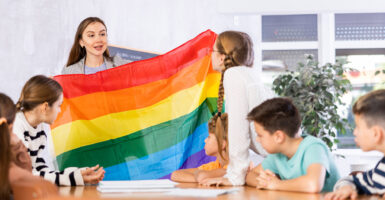 A teacher holds up a gay pride flag in an elementary school classroom