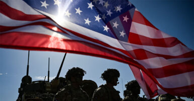 Soldiers under an American flag with the sun shining through it