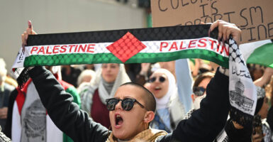 Woman with short hair holds up a banner that says “Palestine” while protesters stage a street demonstration in favor of Hamas and Palestine