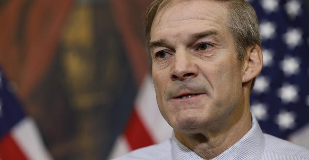 Jim Jordan in a dress shirt stands in front of an American flag