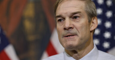 Jim Jordan in a dress shirt stands in front of an American flag
