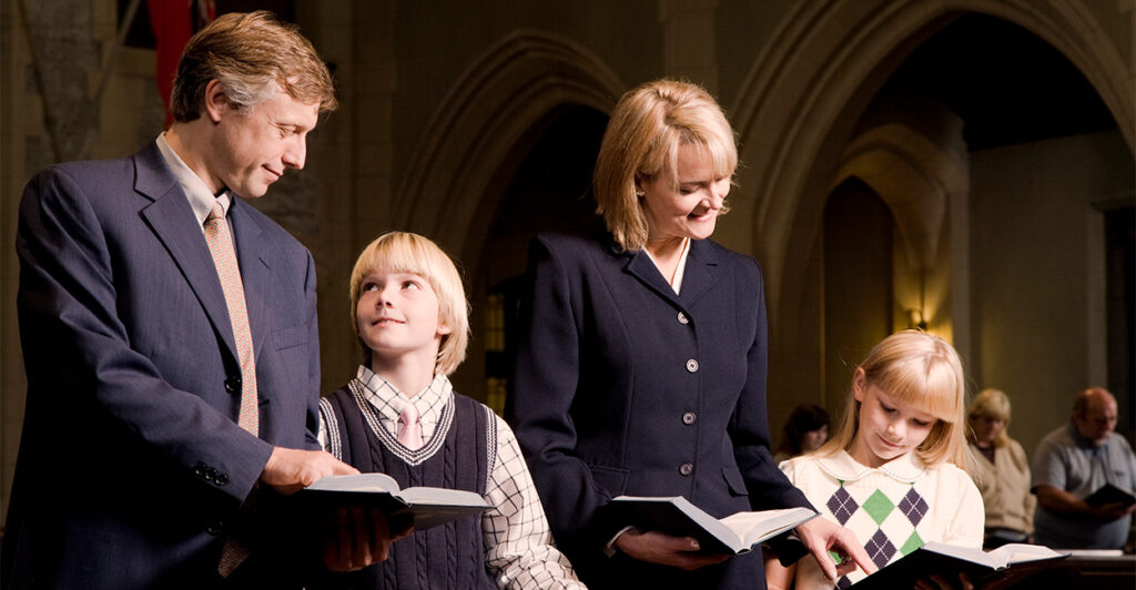 A father, a mother, and their young son and daughter standing in a pew at a church