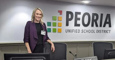 School board member Heather Rooks stand in a meeting room with the Peoria Unified School District sign on the wall behind her.