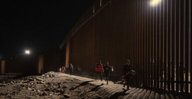 Illegal aliens walk along the border wall fence at night in Yuma, Arizona.