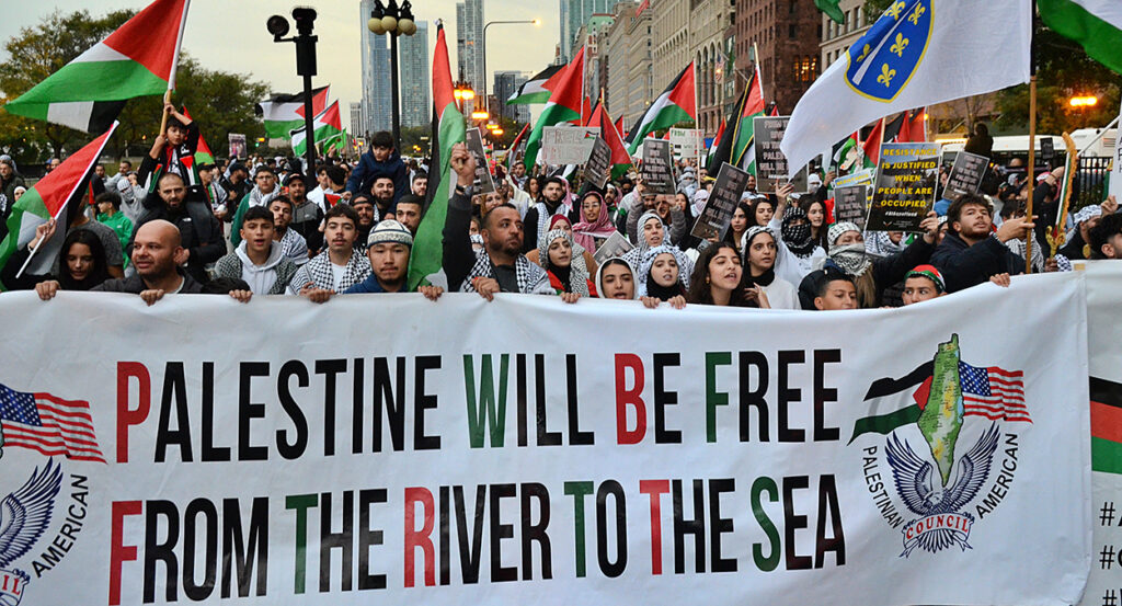 Pro-Palestine protesters march behind a banner reading "Palestine will be free from the river to the sea."