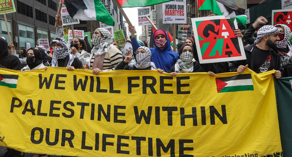 Protesters hold signs reading "We will free Palestine within our lifetime" and "honor our martyrs"
