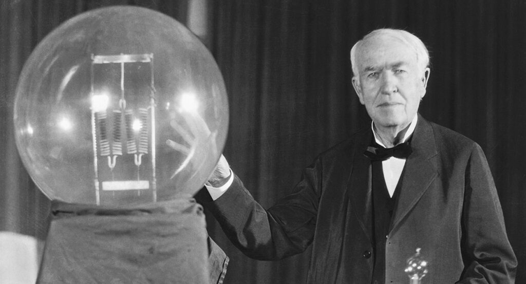Thomas Edison puts his hand on a lightbulb