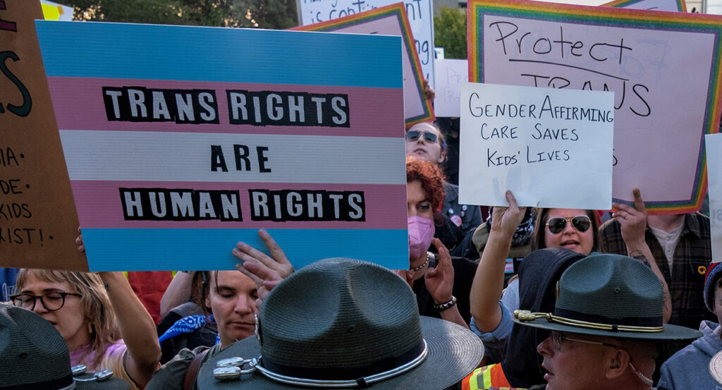 Protesters hold signs reading "trans rights are human rights" and "gender affirming care saves kids' lives."