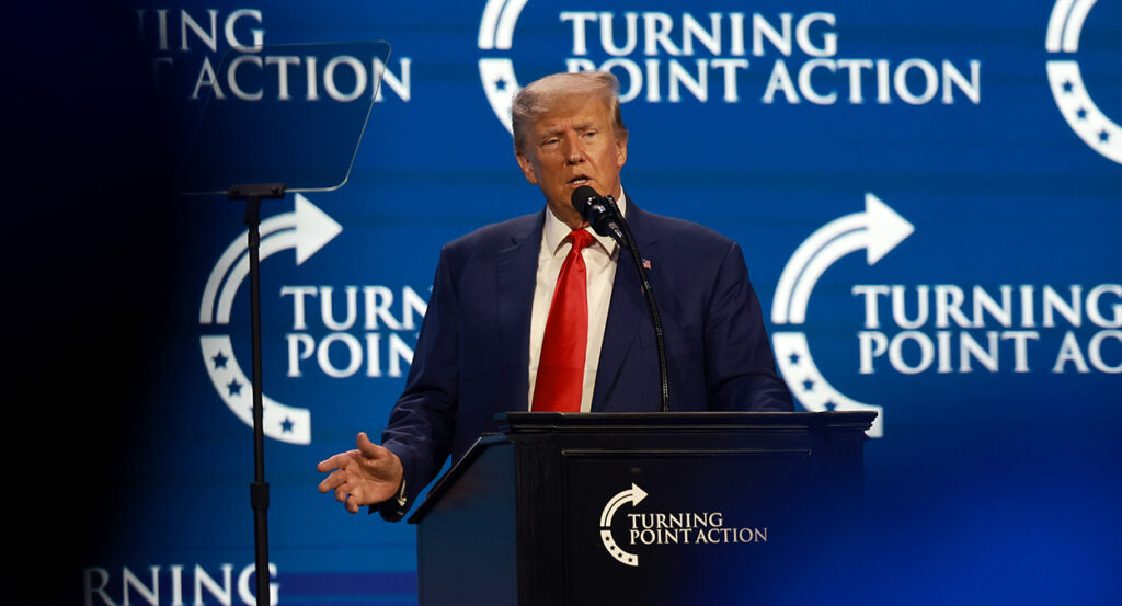 Former President Donald Trump speaks in front of a Turning Point USA logo