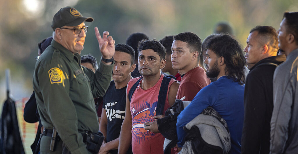 a border partrol agent speaks with migrants