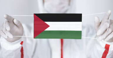 Doctor in surgical gear holding up a mask imprinted with the Palestinian flag