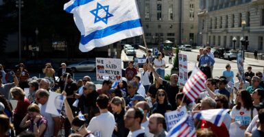 people gather for a rally in Washington D.C., waving Israel's flag above them