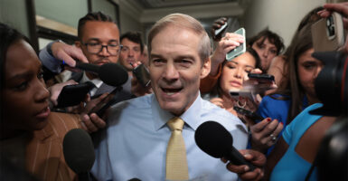 Rep. Jim Jordan smiling and talking to a crowd of reporters with microphones in his face