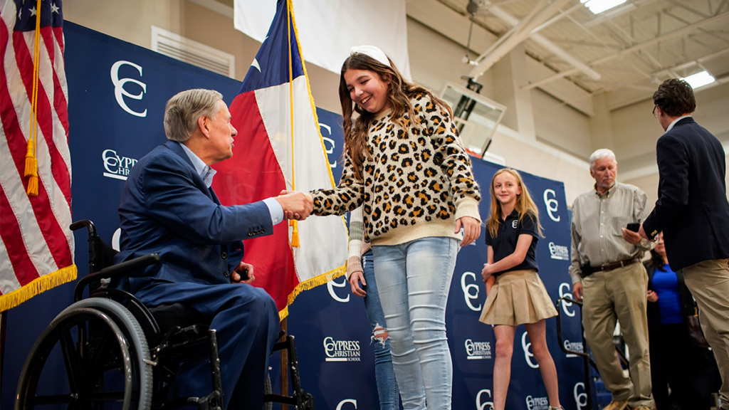 Gov. Greg Abbott in a wheelchair shaking hands with a young student at a rally