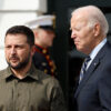 Volodymyr Zelenskyy wears green cargo outfit, stands next to Joe Biden who wears a dark blue suit.