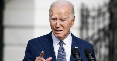 Joe Biden squints at the camera and points while wearing a blue pin-stripe suit with an American flag pin.