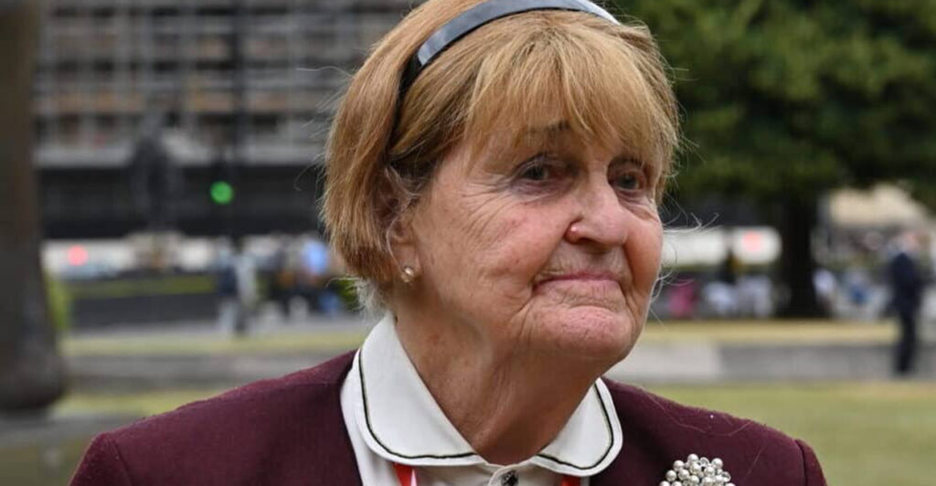 Baroness Caroline Cox stand outside wearing a white blouse and maroon blazer.