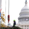 A construction worker stands with a crane in front of the U.S. Capitol
