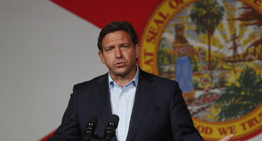 Ron DeSantis in a suit stands in front of the seal of Florida