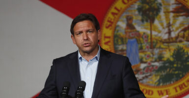 Ron DeSantis in a suit stands in front of the seal of Florida