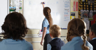 Private school middle schoolers in uniforms in a classroom with one at the white board.