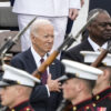 Kamala Harris, Joe Biden, and Lloyd Austin in suits stand in front of soldiers carrying rifles with bayonets.