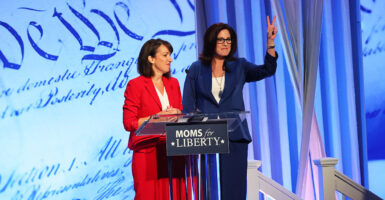 Tina Descovich in red and Tiffany Justice in blue stand before a podium with the Moms for Liberty logo