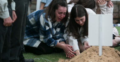 Two women weep at the foot of a grave site.