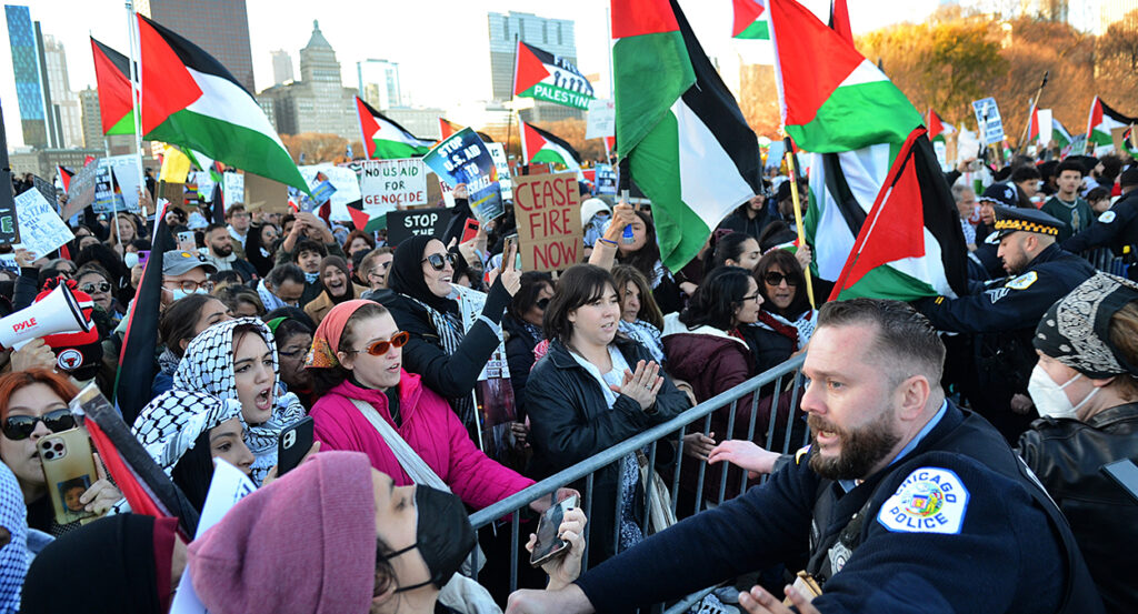 Pro-Palestine protesters press against police in Chicago, holding Palestine flags and signs reading "Ceasefire now"