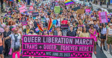 Activists in rainbow flags and various states of dress march with a 