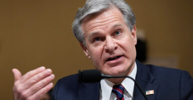 Christopher Wray, wearing a suit, speaks into a microphone at a hearing.
