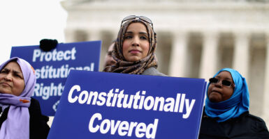 Zainab Chaudry in a headscarf holds a sign in front of the Supreme Court