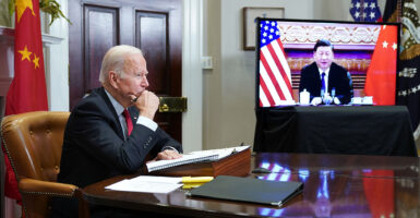 Joe Biden sits at a desk with Xi Jinping displayed on a screen behind him.