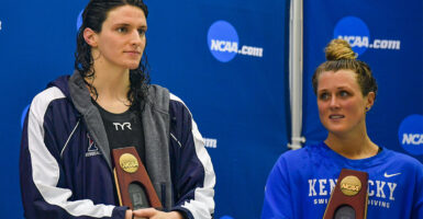 Lia Thomas and Riley Gaines stand together with trophies at an NCAA swim tournament