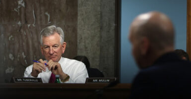 Sen. Tuberville sits behind a desk in a white shirt and a tie.