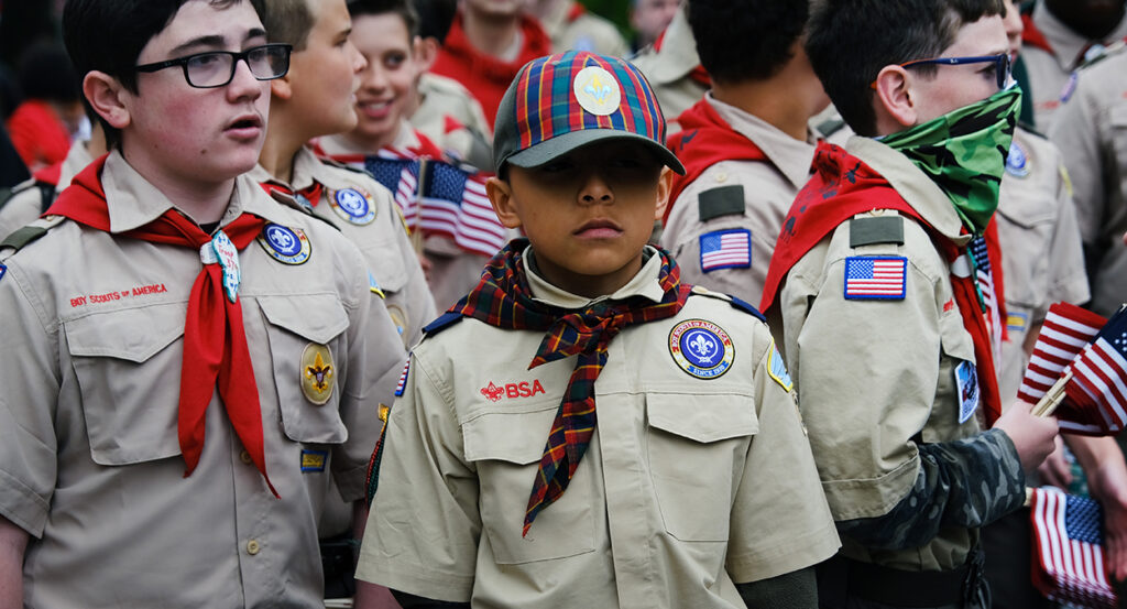 Boy scouts stand around aimlessly in uniform with American flags