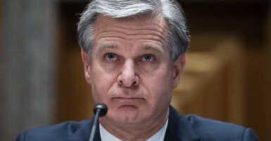 Christopher Wray in a blue suit speaks in front of a microphone
