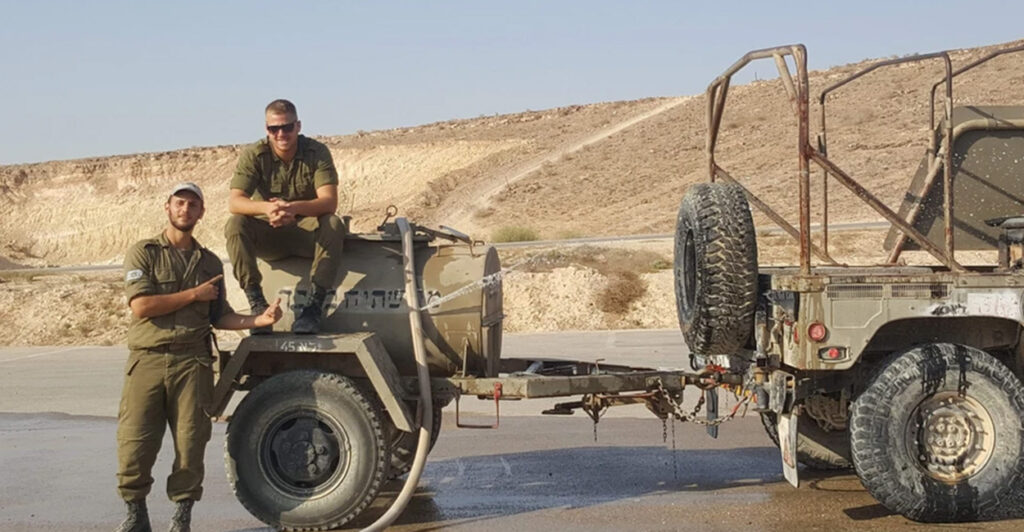 David Newman is seen sitting on the hood of a military vehicle next to another IDF soldier.