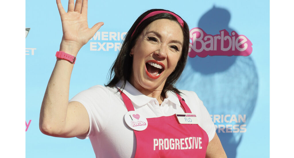 Flo from Progressive in pink in front of a Barbie logo