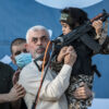 Yahya Sinwar holding a young boy and an AK-47 military rifle on a stage.