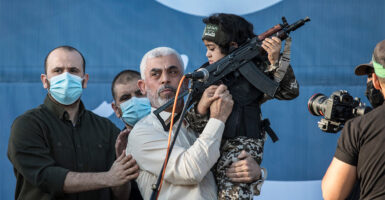 Yahya Sinwar holding a young boy and an AK-47 military rifle on a stage.