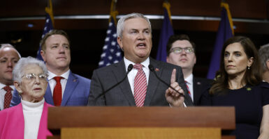 James Comer in a grey suit with a striped tie lifts his left forefinger in the air.